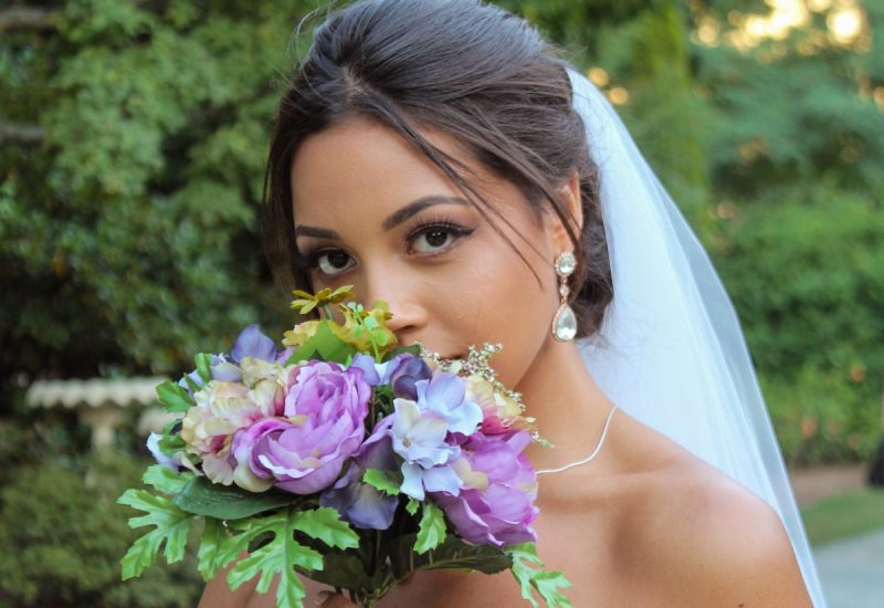 Bride in a white gown holding a flower bouquet, captured in soft, natural light on her wedding day.